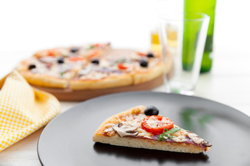 fresh pizza in a rustic Italian style with jerky olives mushrooms and three kinds of cheese on a light wooden background with a bottle of cold beer