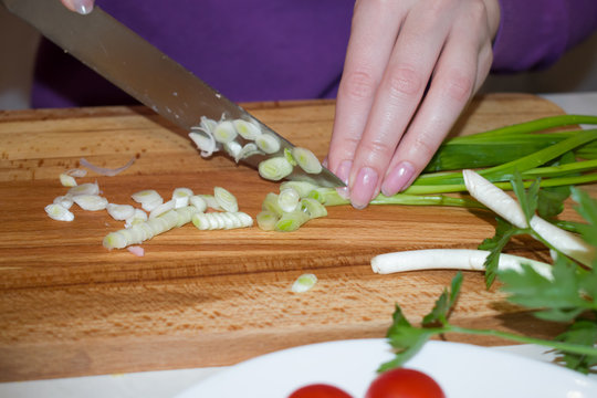 Beautiful female hands with a knife sliced green onions for the salad.