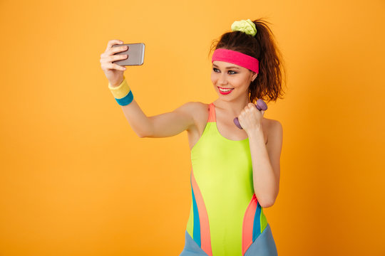Smiling fitness woman with dumbbell making selfie using cell phone