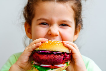 Happy hungry child (girl) eating healthy vegan burger.