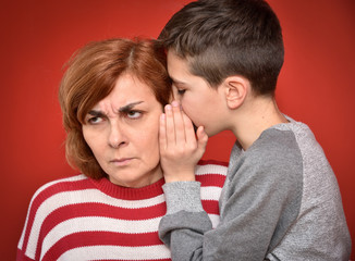Young boy whispering secret into ears of angry mother