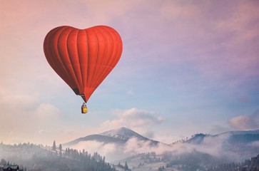 Red air balloon heart shape against blue and pink pastel sky in a sunny bright morning. Foggy mountains in the background. Romantic postcard background on Valentine's Day. Travel and recreation theme © Goinyk