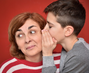 Young boy whispering secret into ears of smiling mother