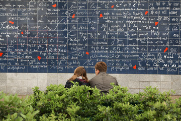 PARIS, FRANCE - APRIL 16,  2016:  Young couple sitting near I Love You wall on Monmartre.