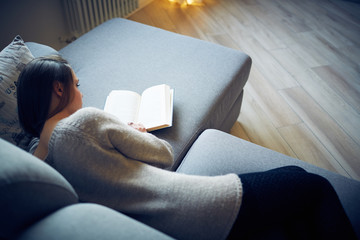 Ragazza legge libro sul divano a casa