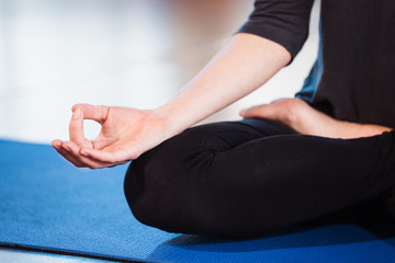 Yoga girl meditating indoor and making a zen symbol with her hand. Closeup of woman body in yoga pose on a green mat