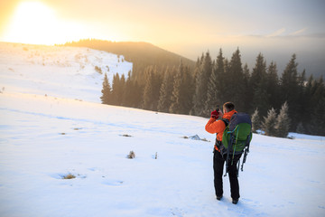 Hiker in winter mountains. Man with backpack trekking in mountains. Winter hiking. Beautiful sunrise in the winter mountains.