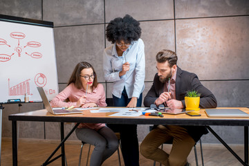 Multi ethnic coworkers working together with documents and laptop at the workplace with whiteboard on the grey wall background