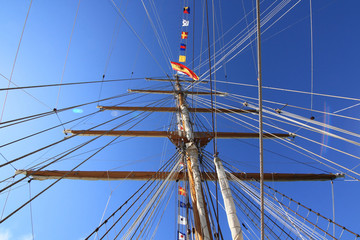 A sailing ship mast with ropes against blue sky and patch of reflected light from sun