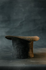 Worn damaged old and vintage black top hat isolated against dark background