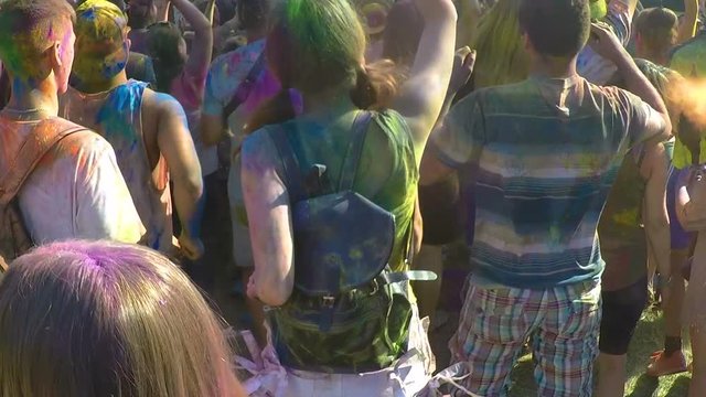 Outdoor music festival audience covered in colorful paint jumping at concert