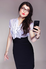 Beautiful brunette caucasian business woman in classic dress and glasses looks like teacher make selfie. neutral grey background