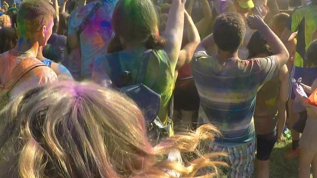 Active young men and women covered in color paint jumping to music at festival