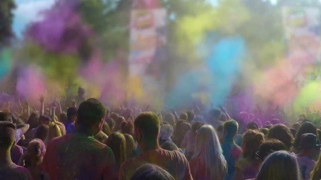 Atmosphere at outdoor color festival, many people throwing powder dye in air
