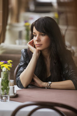 Brunette beautiful stylish caucasian woman in casual outfit on a walk on european city street sitting at the cafe waiting