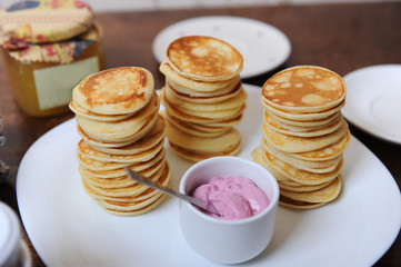 Pancakes with berry sauce on a white plate. Bank of jam in the background