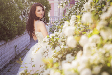 Beautiful brunette woman bride in a garden park in white wedding dress, curly hairstyle and a smile. warm weather, outdoors. copy space