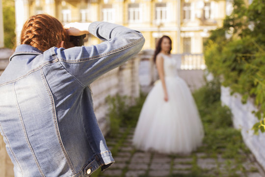 Photographer capture a Beautiful brunette woman bride in a garden park in white wedding dress, curly hairstyle and a smile. warm weather, outdoors. Backstage