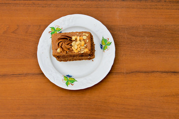 Piece of cake with nuts on plate on wooden table. Top view