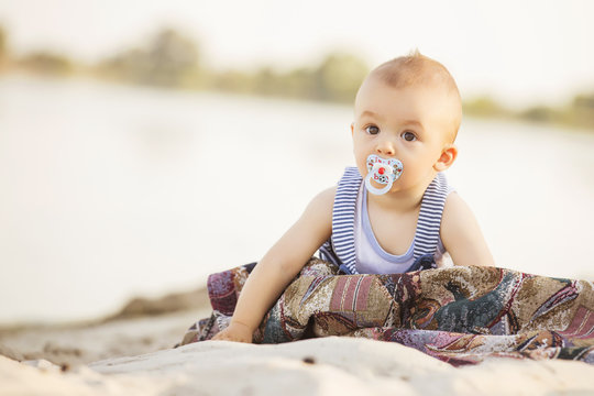 Happy smiling cute little infant baby on a seashore near water in blue and white and red outfit: t-shirt and shorts. Summer. Copy space