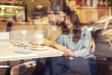 Cute brunette loving couple in cozy warm sweaters on a date at the cafe having fun hugging. cold autumn, winter or spring day, european city. indoors