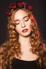 Fototapeta premium Beautiful blonde model woman with curly hairstyle and black cat eyes, in black dress with circlet (wreath) of flowers (roses) on her head. her eyes closed, showing make up. black background. close-up