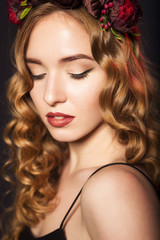 Beautiful blonde model woman with curly hairstyle and black cat eyes, in black dress with circlet (wreath) of flowers (roses) on her head. her eyes closed, showing make up. black background. close-up