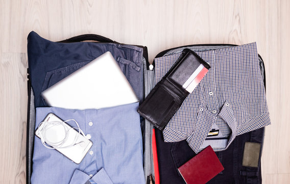 Open traveler's bag with men clothing, accessories, credit cards, wallet, passport and smart phone. Travel and vacations concept. 