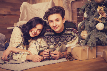 Beautiful brunette caucasian romantic loving couple in cozy warm sweaters in the cabin on a christmas new year eve, smiling, kissing, having fun with each other. Dim dark night light, toned image