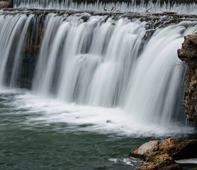 Obraz premium Waterfall among boulders on a warm winter day makes a scenic view.