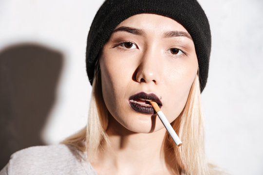 Portrait of beautiful young woman hipster in hat smoking cigarette