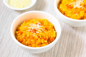 Fresh homemade carrot risotto made with pureed carrot and roasted carrot pieces, garnished with grated cheese, photographed with natural light (Selective Focus, Focus in the middle of the risotto)