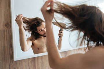 Man looking at the mirror and drying hair with hairdryer