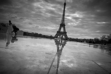 View of the Eiffel Tower from the Trocadero. Reflection tower in wet rain stone pavement. Assistant photographer corrects the dress the bride during the wedding photosessions. BW photo. France. Paris.