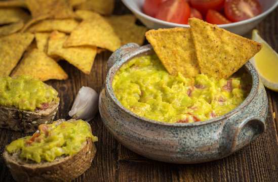 Guacamole in home crafted bowl  with tortilla chips on natural wooden desk.