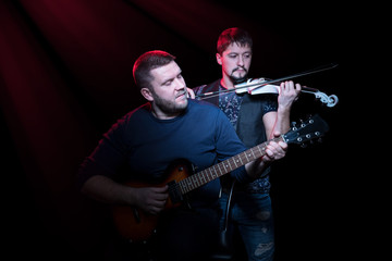 Fototapeta premium Two bearded men playing on electric guitar and electro violin on a black background