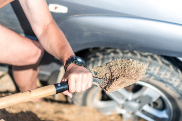a man digs a car stuck in the sand, throwing sand shovel out from under the car