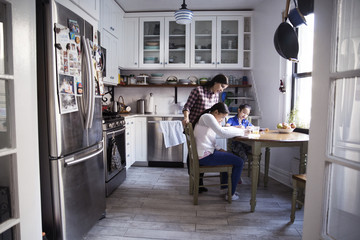 Mother assisting daughters for studying at table in kitchen
