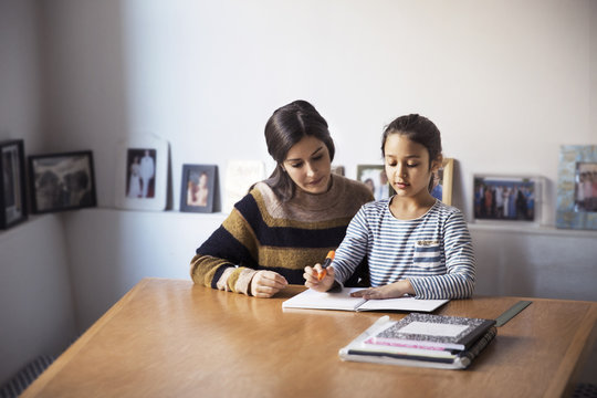 Mother assisting daughter for studying while sitting at table