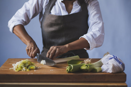 Midsection Of Woman Cutting Scallions In Kitchen Against Wall