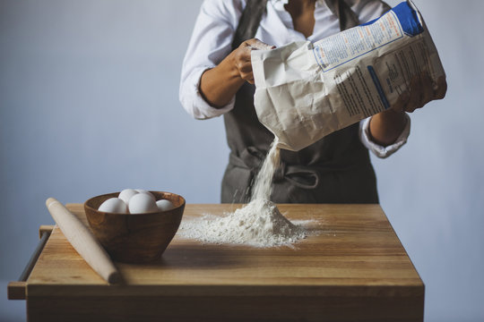 Midsection of woman removing flour from packet on table against wall