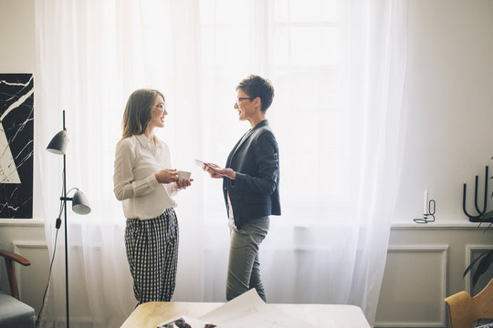 Businesswomen talking while standing by curtain in office