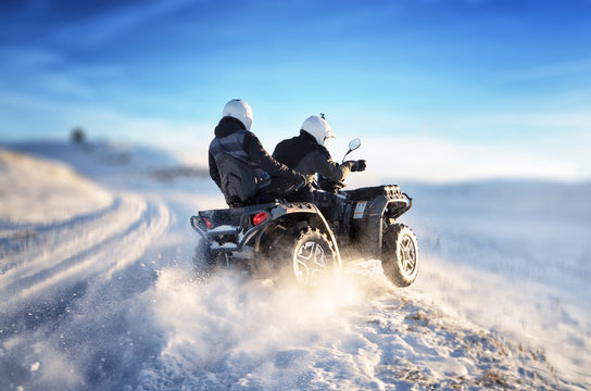 Quad bike in motion, ride on top of the mountain on snow. People riding quad bike on mountain at sunset