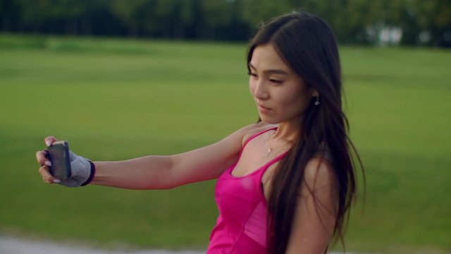 Sport woman taking selfie in park. Asian woman selfi outdoors. Fit girl selfie photo on mobile phone at meadow. Closeup of fitness woman posing for selfie portrait. Fit girl using phone for selfie