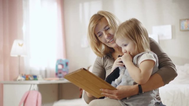 Cute Little Girl Sits on Her Grandmother's Lap and They Use Tablet Computer. Slow Motion. Shot on RED EPIC-W 8K Helium Cinema Camera.