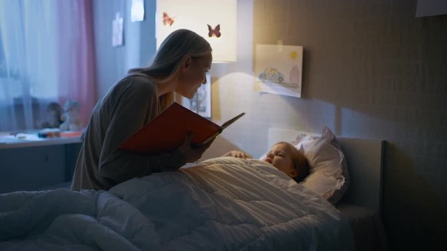 Young Loving Mother Reads Bedtime Stories to Her Little Beautiful Daughter who Goes to Sleep in Her Bed. Shot on RED EPIC-W 8K Helium Cinema Camera.