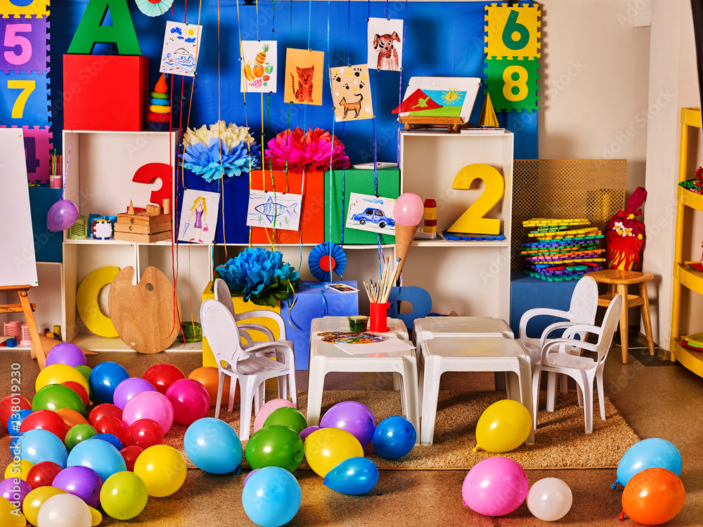 Wall mural Kindergarten interior decoration child picture on wall. Preschool class waiting kids. Colour balloons on floor. Playroom with white table. Art room education children's creativity. Mess in classroom.