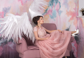 beautiful young model with open angel wings sitting on sofain the studio. white background
