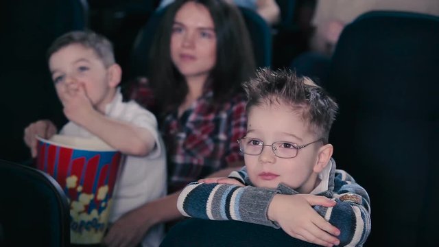 The boy in glasses are watching the movie in the cinema