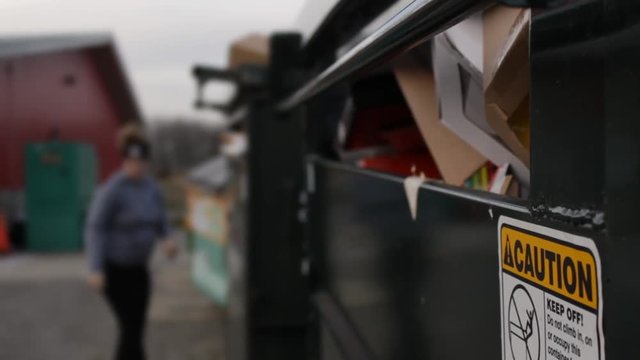 Woman recycles cardboard into dumpster
